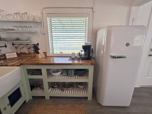 A kitchen with a white refrigerator, wooden countertop, and a window with blinds. - Old Florida Fish Camp Cedar Key (Cedar Key)