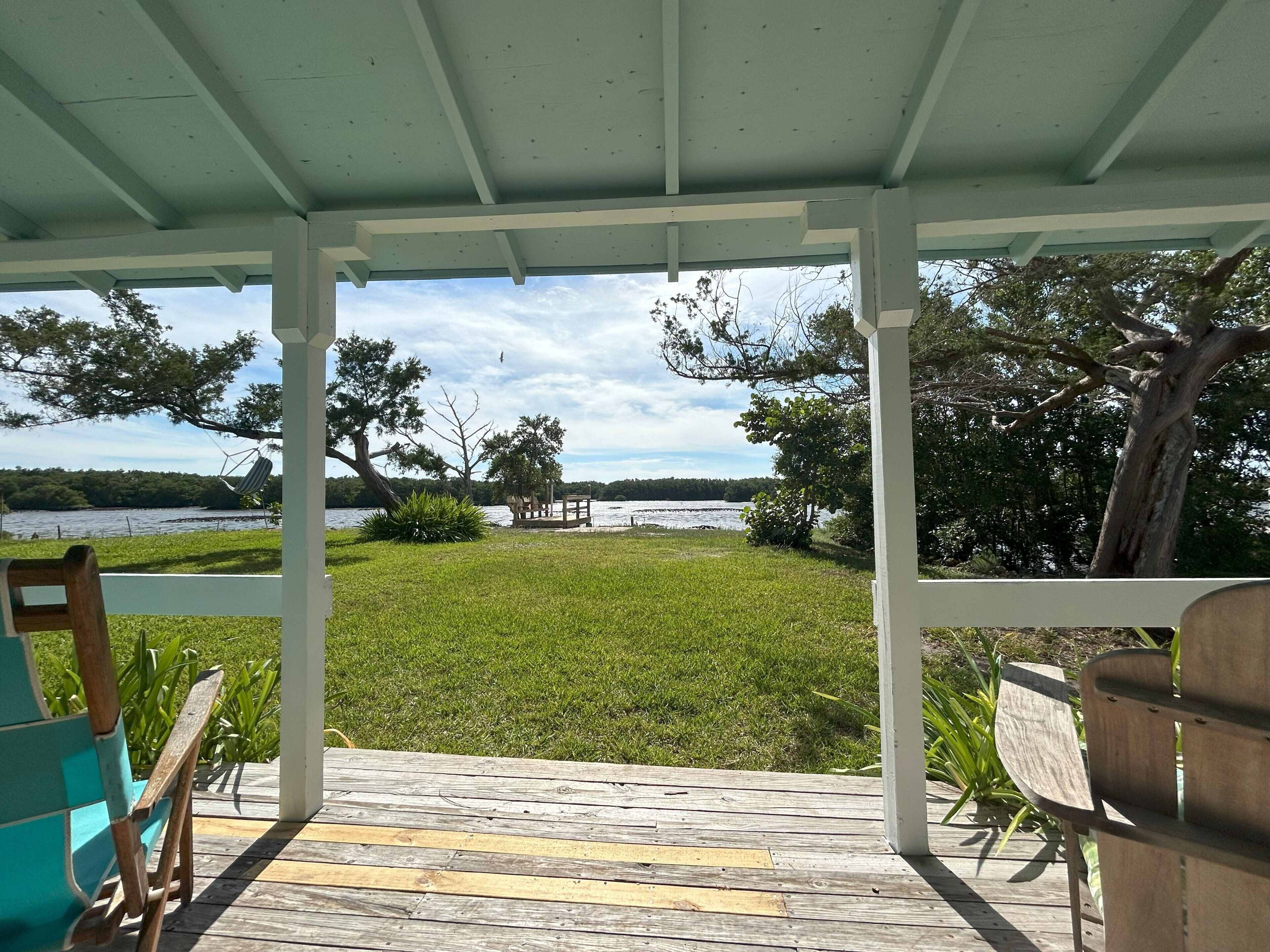 A covered outdoor area with a view of a lake, wooden deck, and chairs.