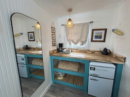 Una cocina compacta con pared espejada, encimera de madera y un refrigerador blanco pequeño.