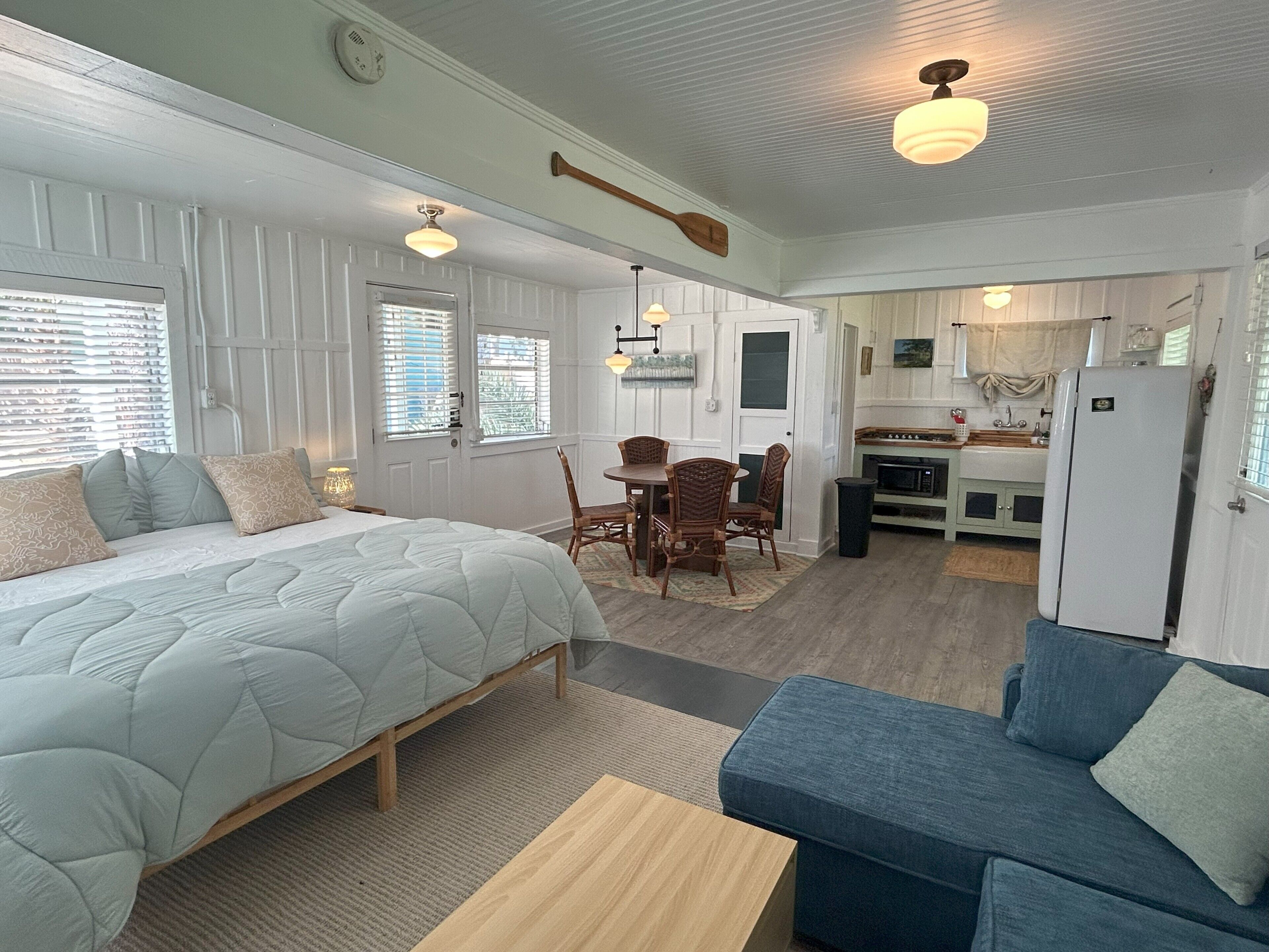A bedroom with a bed, a dining table with chairs, a kitchenette, and a living area with a sofa.