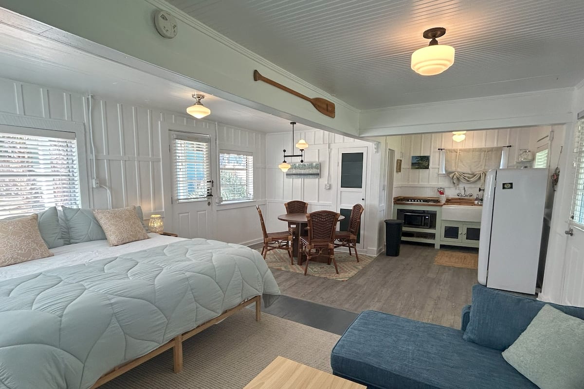 Un dormitorio con cama, una mesa de comedor con sillas, una kitchenette y una sala de estar con sofá.