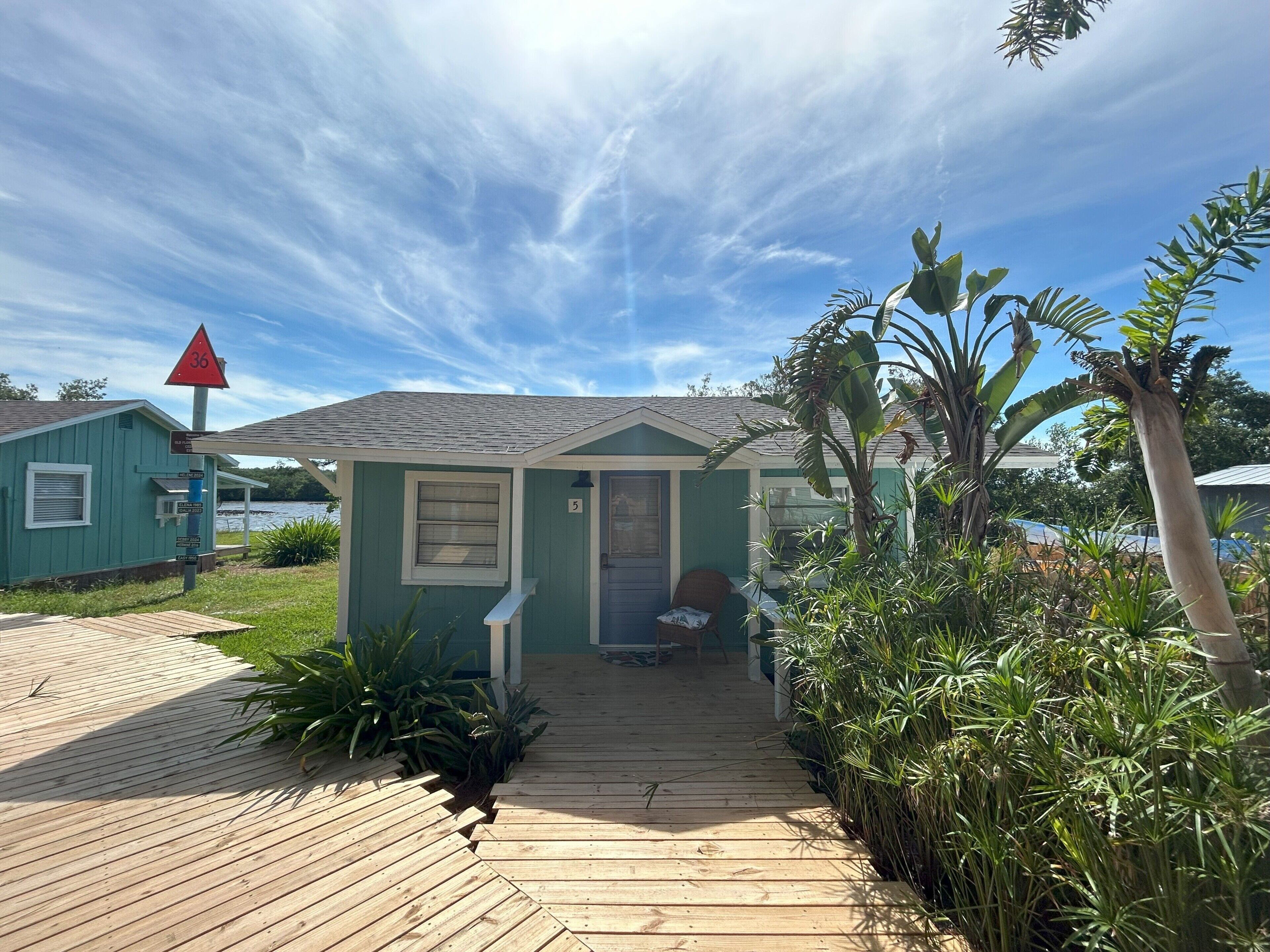 A small, single-story building with a wooden deck leading to the entrance, surrounded by lush greenery.