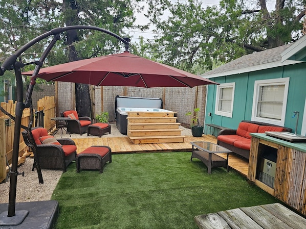 A backyard with a hot tub, outdoor furniture, a wooden deck, and a green lawn.