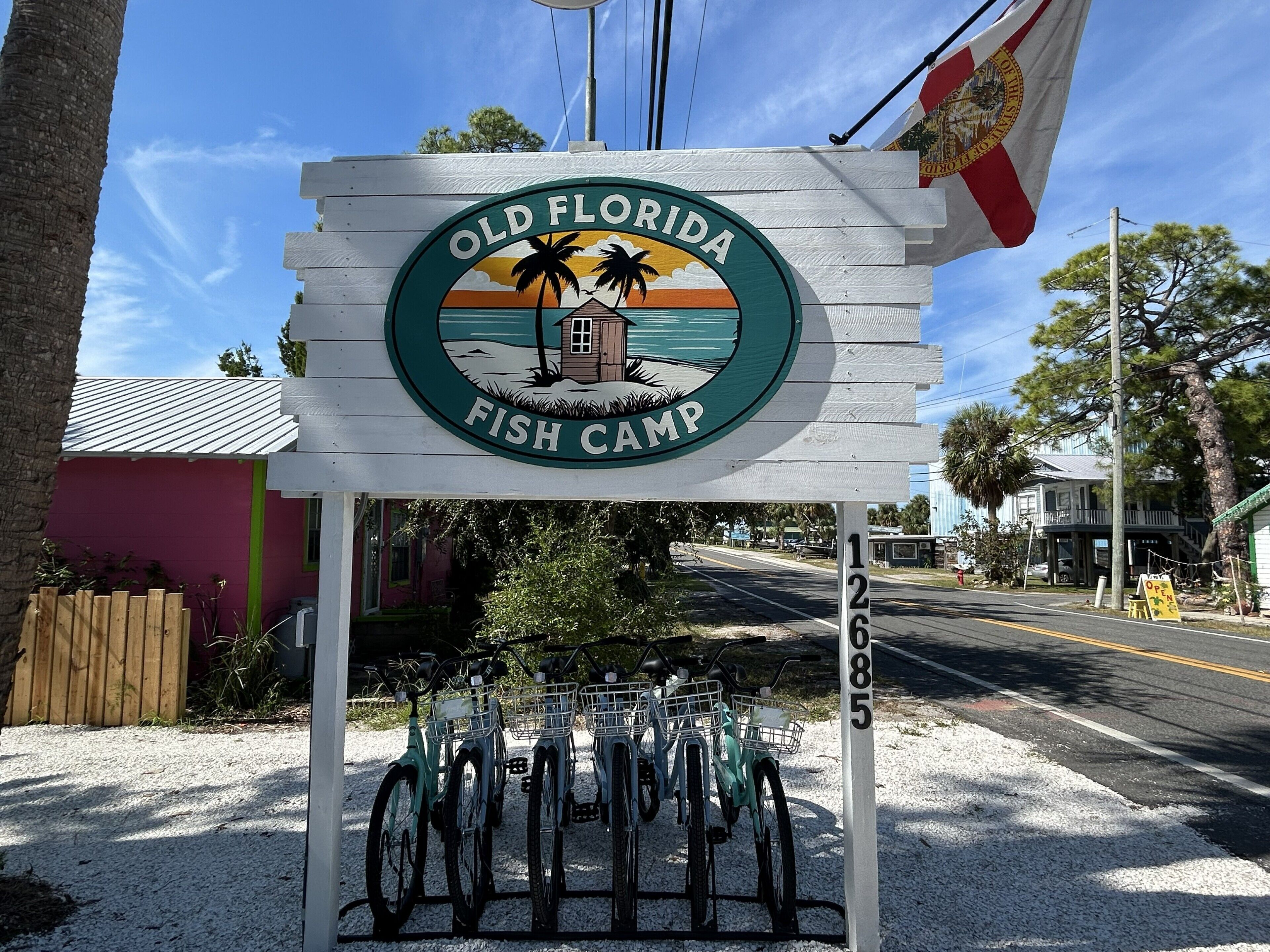 Een houten bord met 'Old Florida Fish Camp' en een afbeelding van een palmboom en een zonsondergang.