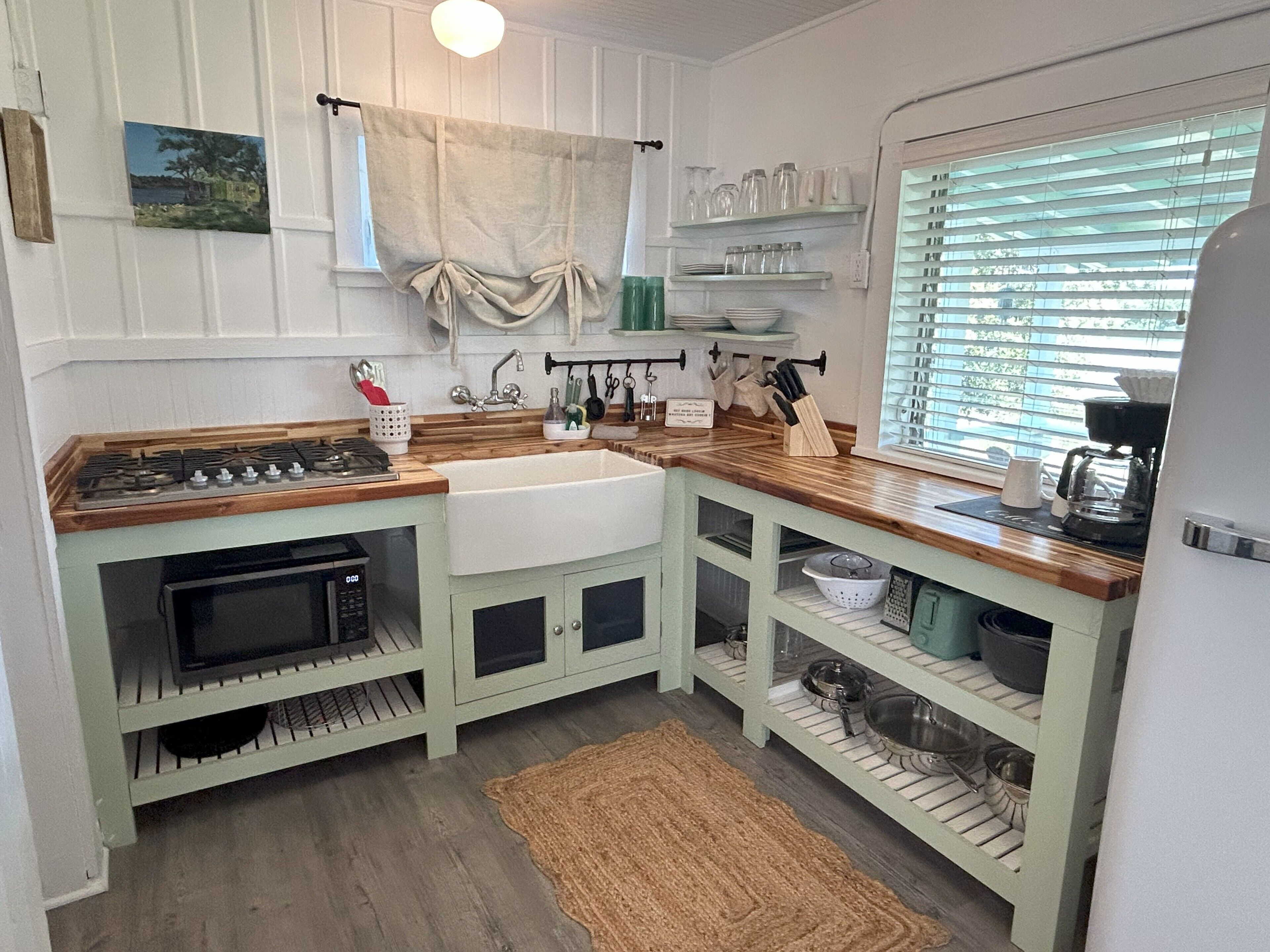 Une cuisine avec un plan de travail en bois, un évier, une cuisinière et une fenêtre avec des stores.