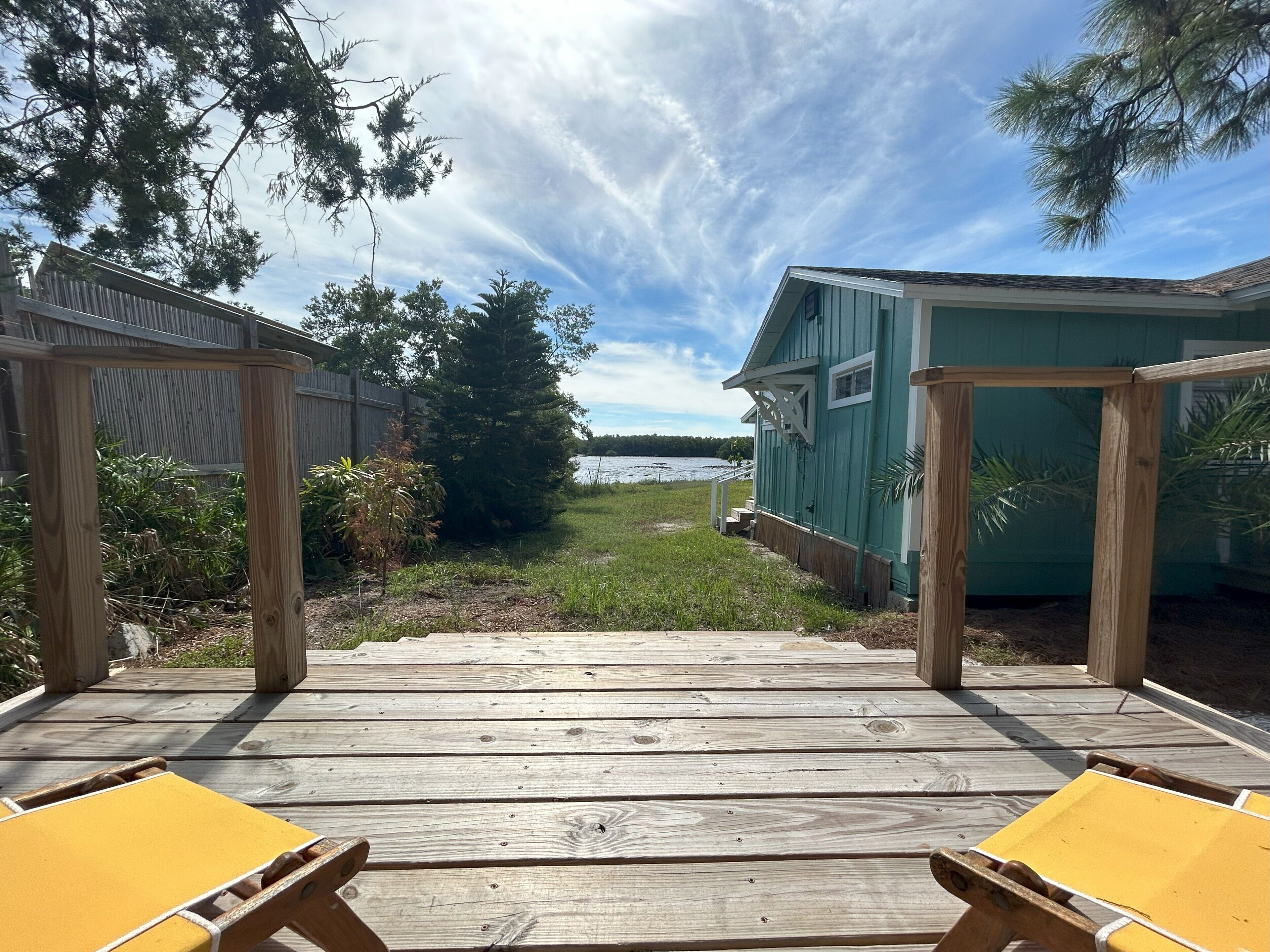 Una terraza de madera con sillas reclinables amarillas, una pérgola de madera y vistas a un lago.