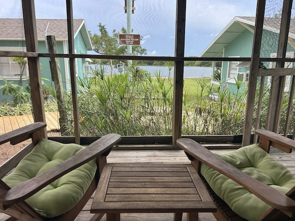 Eine Holzterrasse mit zwei Bänken, einem Tisch und Blick auf einen See und Gebäude.