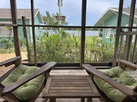 Una terraza de madera con dos bancos, una mesa y vistas a un lago y edificios.