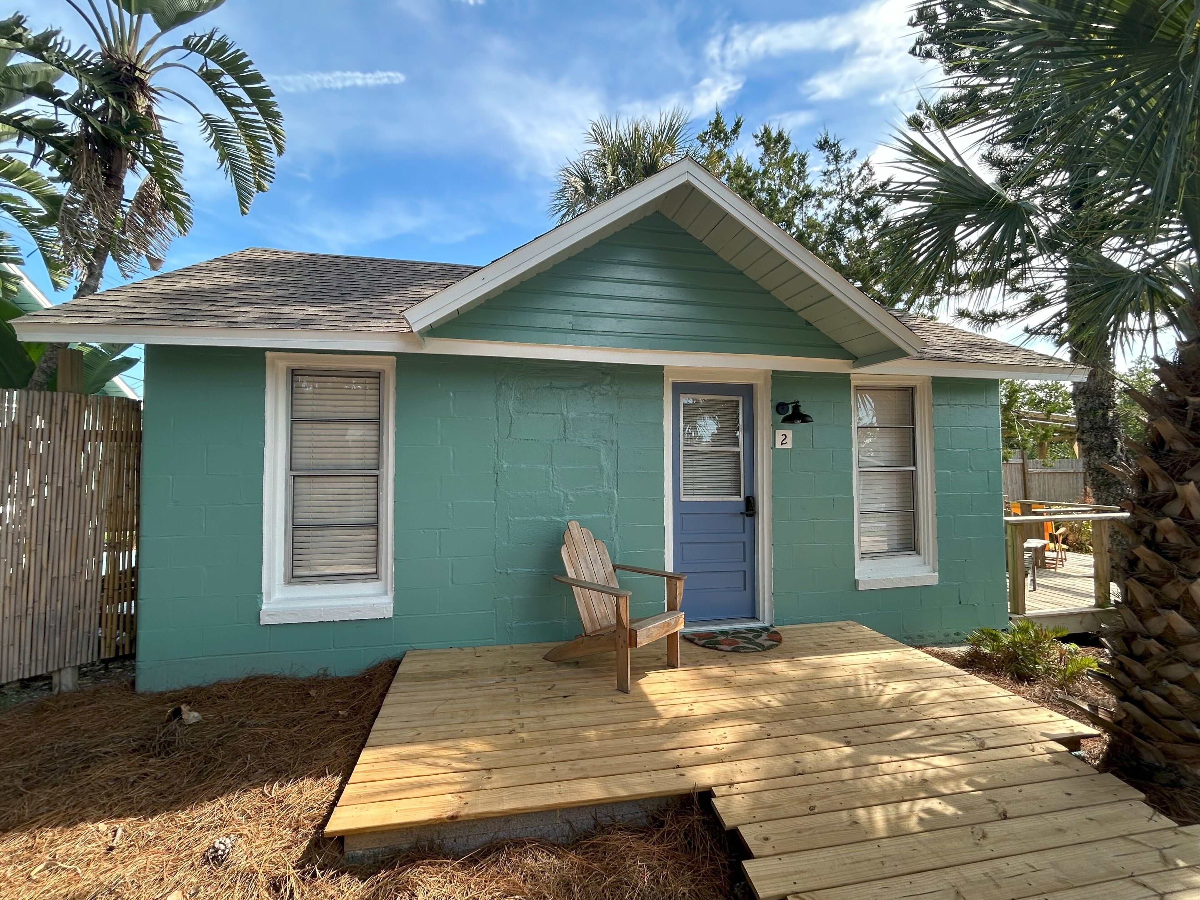 A small house with a green exterior, a wooden deck, and a single door.