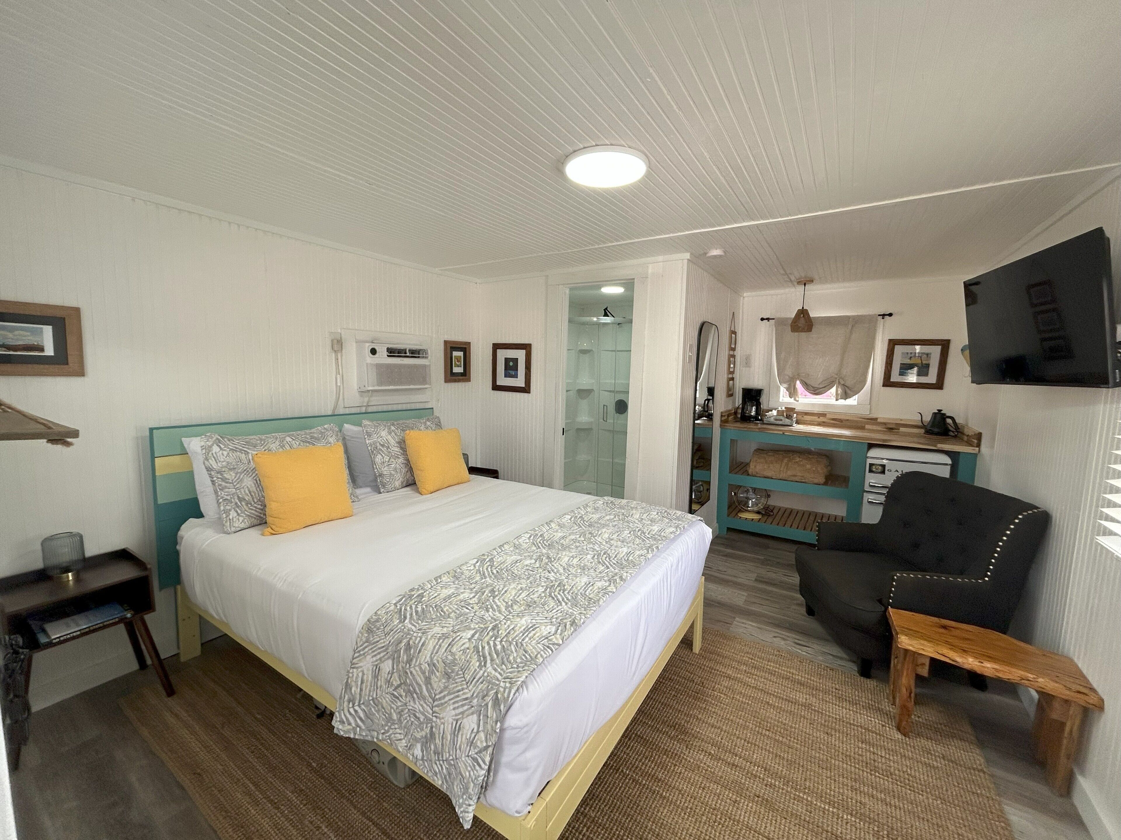 A bedroom with a bed, a desk, a chair, a TV, and a bathroom.