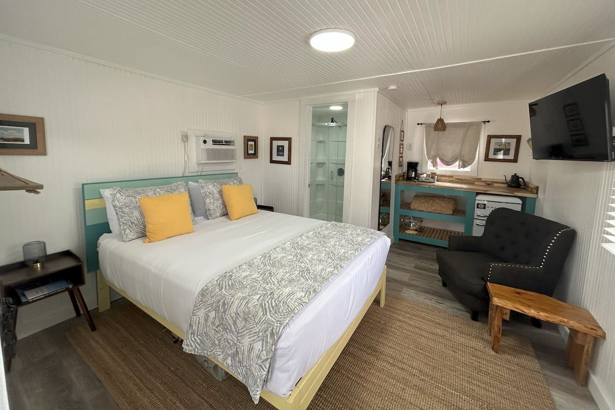 Un dormitorio con cama, escritorio, silla, televisor y baño.