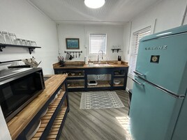Una cocina compacta con microondas, lavamanos y refrigerador azul.