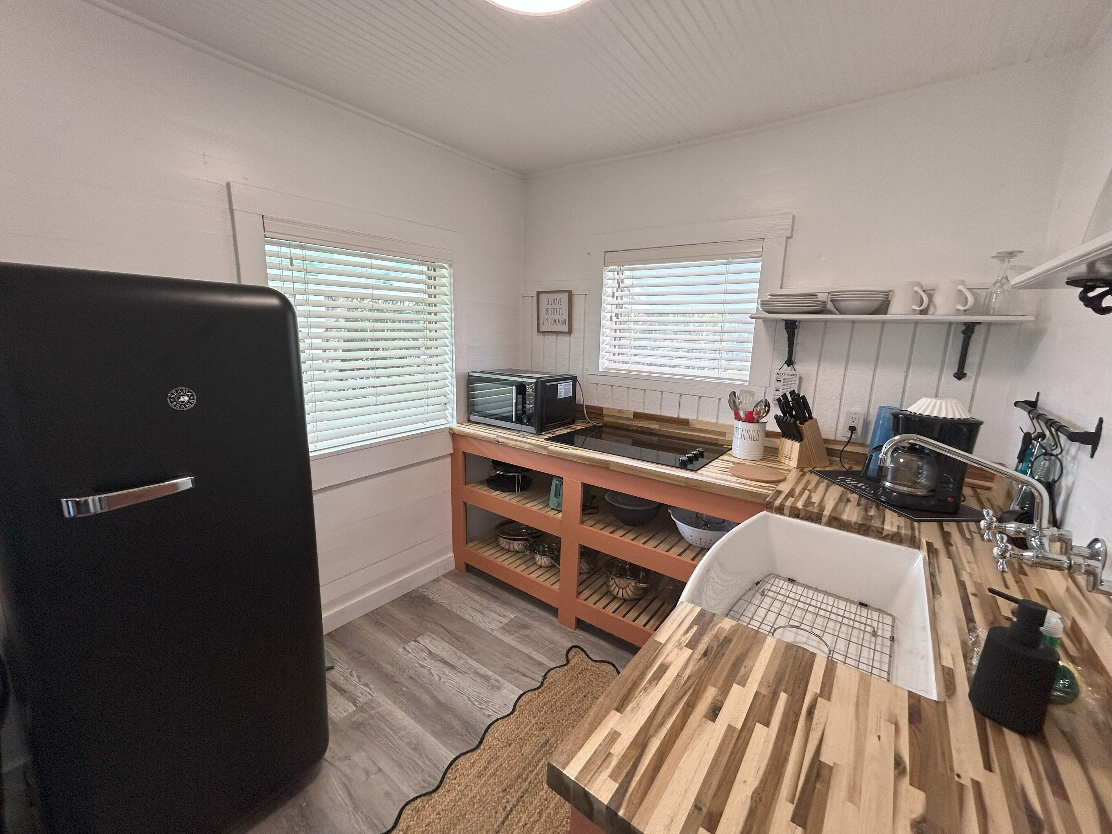 A compact kitchen with a refrigerator, microwave, sink, and wooden shelves.