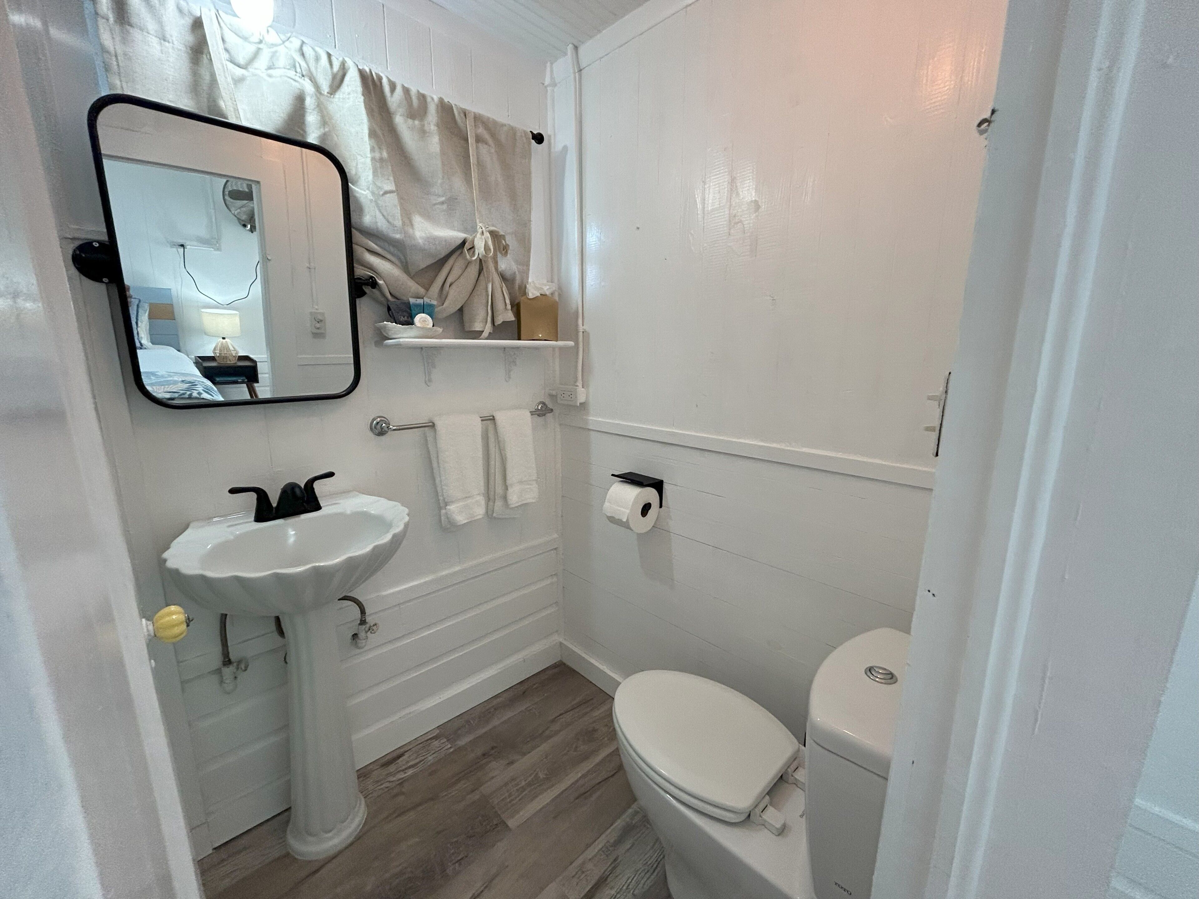 Un bany amb un lavabo blanc, mirall, vàter i terra de fusta.