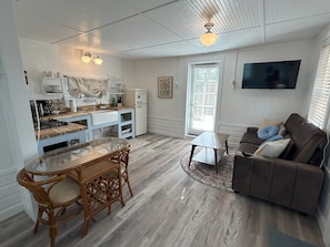 Un espacio habitable compacto con cocina, comedor y zona de estar con sofá y televisor.
