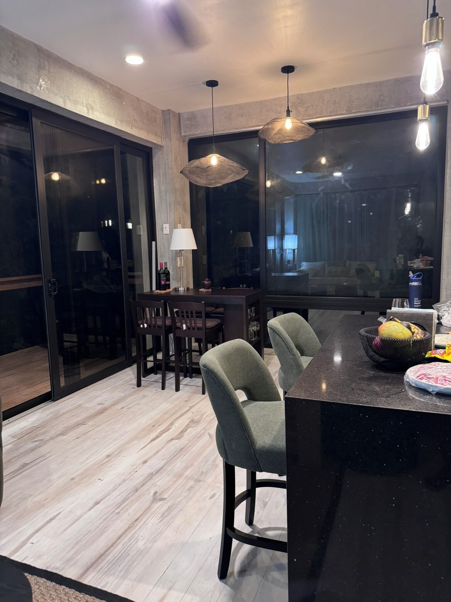 A modern kitchen with a bar area, wooden flooring, and large windows.