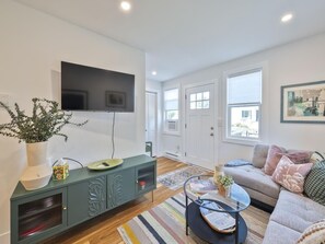 Ein Wohnzimmer mit Flachbildfernseher, einem grünen Schrank, einer Couch und einem Couchtisch.
