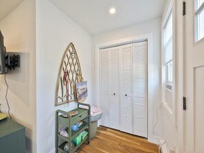 Ein Zimmer mit einem weißen Schrank, einem an der Wand befestigten Regal mit einem Bilderrahmen und einem Wagen mit verschiedenen Gegenständen.