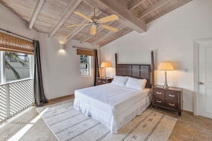 Ein Schlafzimmer mit einem Bett, zwei Nachttischen, einem Deckenventilator und einem Fenster mit Jalousien.