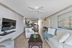 Ein Wohnzimmer mit Flachbildfernseher, Deckenventilator, Couchtisch, weißes Sofa und einem Gemälde an der Wand.