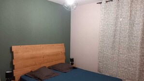 Een kamer met een houten bed, een blauwe matras, twee kussens, een nachtkastje met een lamp en een kamerbedekking met een patroon.