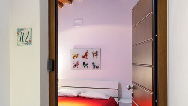 A bedroom with a red bedspread, a white bedside table, and a wall-mounted artwork. - Lilum B&B Villa Patrizia - Mamo Florence (Itri)