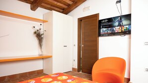 A room with a bed, a chair, a shelf with decorative items, a wooden door, and a wall-mounted TV displaying a game. - Lilum B&B Villa Patrizia - Mamo Florence (Itri)