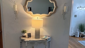 Ein Zimmer mit einer verzierten Konsole, einem Wandspiegel, einer Lampe und einer Topfpflanze.