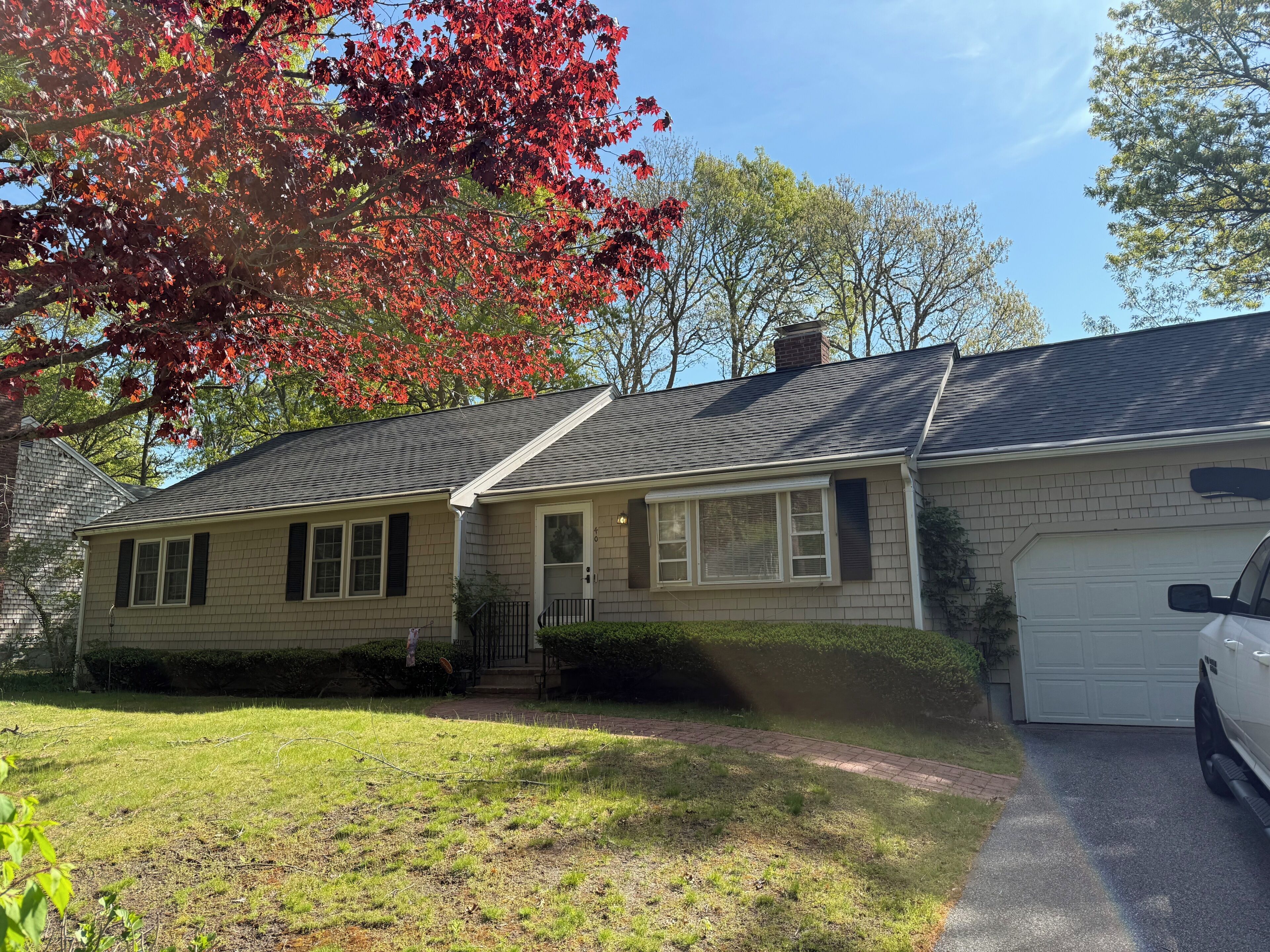 A single-story home set in a peaceful neighborhood, framed by mature trees displaying vibrant spring foliage and accessed by a private driveway.