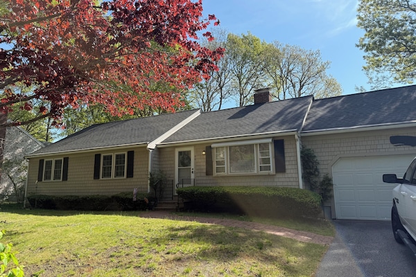 A single-story home set in a peaceful neighborhood, framed by mature trees displaying vibrant spring foliage and accessed by a private driveway.