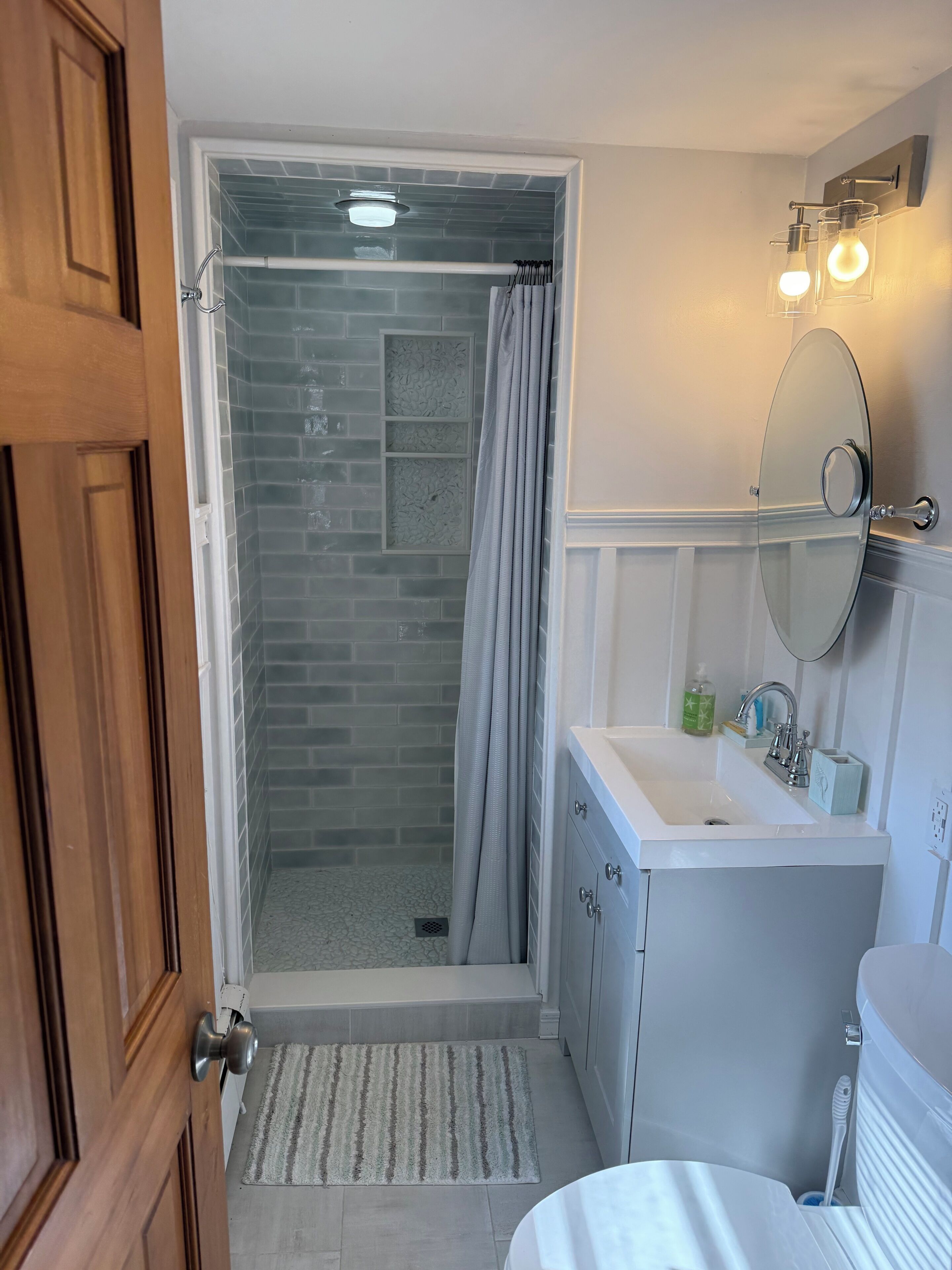 A bathroom with a shower, a sink, a mirror, and a door.
