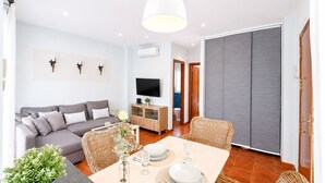 A modern living room with a sofa, dining table, and chairs, a TV, and a sliding door. - Casa Almeida en Conil (Conil de la frontera)