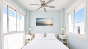 A bedroom with a bed, a ceiling fan, a painting, and two bedside tables. - Casa Almeida en Conil (Conil de la frontera)