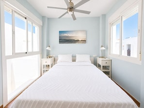 Ein Schlafzimmer mit einem Bett, einem Deckenventilator, einem Gemälde und zwei Nachttischen.
