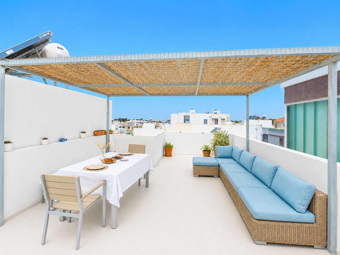 A rooftop terrace with a covered seating area, a dining table, and potted plants.