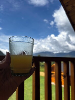 Una mano sosteniendo un vaso de jugo de naranja, con un cielo despejado y nubes al fondo.