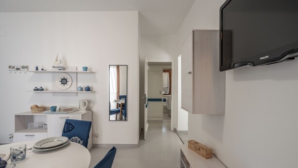 A modern kitchen with white cabinetry, a built-in oven, and a flat-screen TV. - Casa AzzurroLido (Alghero)