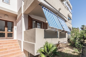 A building with a balcony, a wooden door, and a small garden area. - Casa AzzurroLido (Alghero)
