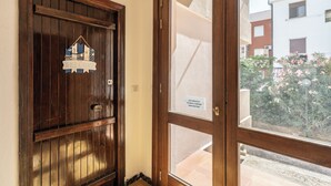 A wooden door with a welcome sign, a glass door with a sign, and a view of a building and garden. - Casa AzzurroLido (Alghero)