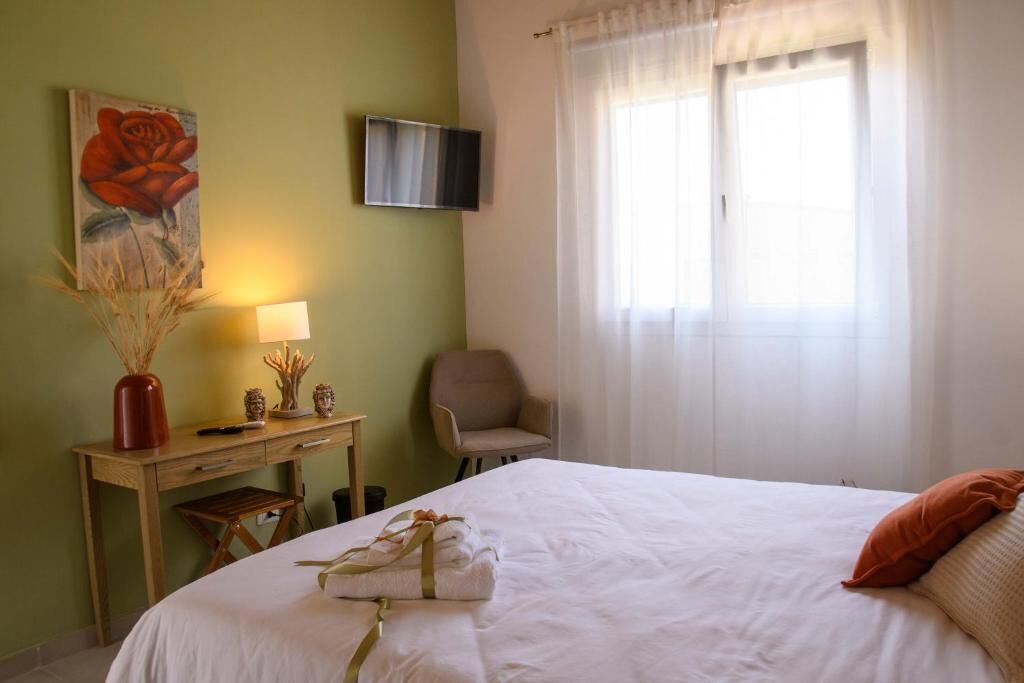 Habitación de hotel con cama, escritorio, silla, televisor montado en la pared y ventana con cortinas.