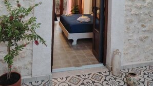 A doorway leading to a bedroom with a bed, a potted plant, and a tiled floor.