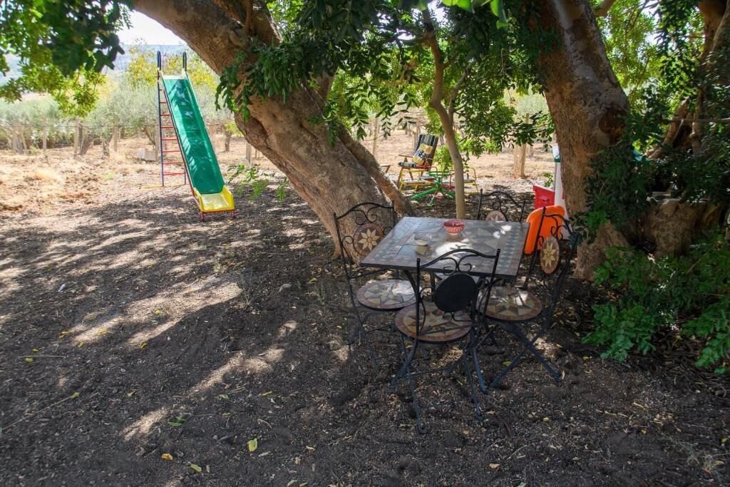 Un'area patio con tavolo e sedie, un'altalena e alberi che offrono ombra.