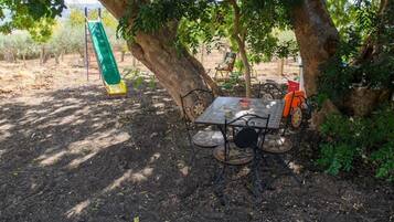 Un'area patio con tavolo e sedie, un'altalena e alberi che offrono ombra.
