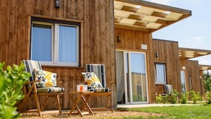 Un edificio moderno de madera con ventanas amplias, asientos exteriores y un patio cubierto.