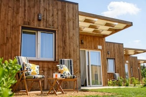 A modern wooden building with large windows, outdoor seating, and a covered patio area.