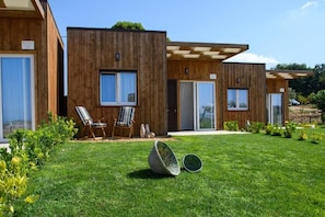 Un edificio moderno de madera con ventanas amplias, una zona de estar exterior cubierta y un césped cuidado.