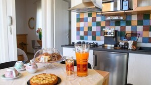 A breakfast table with pastries, a glass of orange juice, and a coffee machine in a modern kitchen with a colorful tile backsplash.