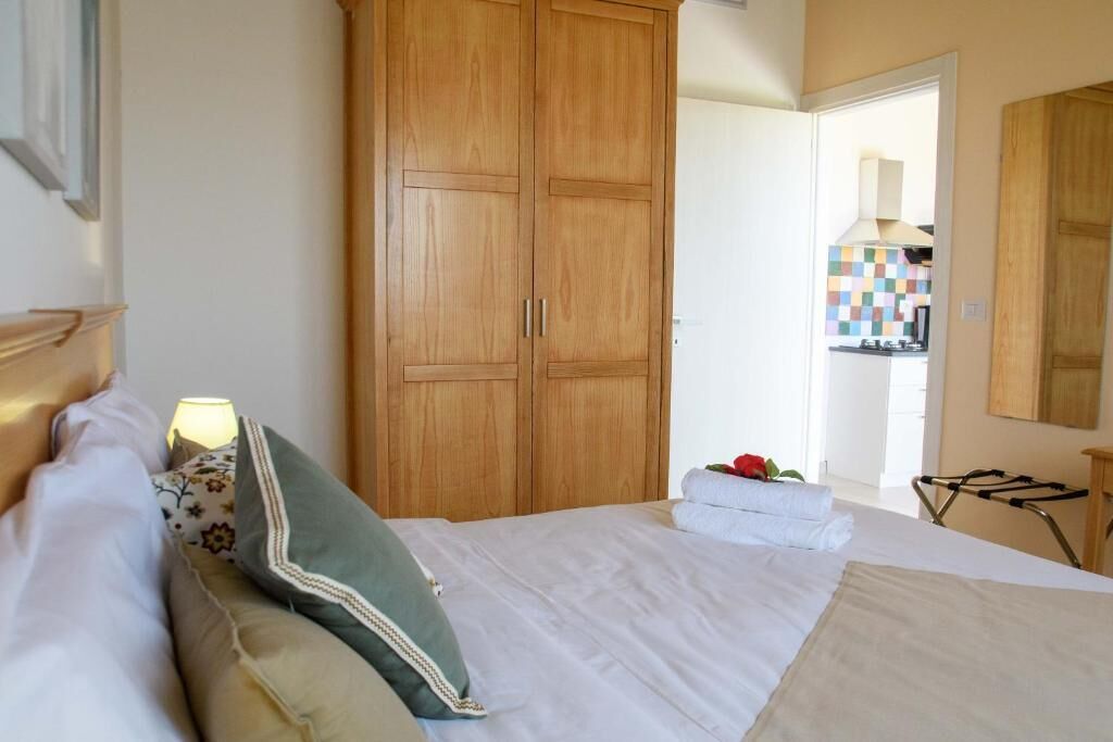 A bedroom with a bed, a wooden wardrobe, a bathroom visible through an open door, and a towel on the bed.