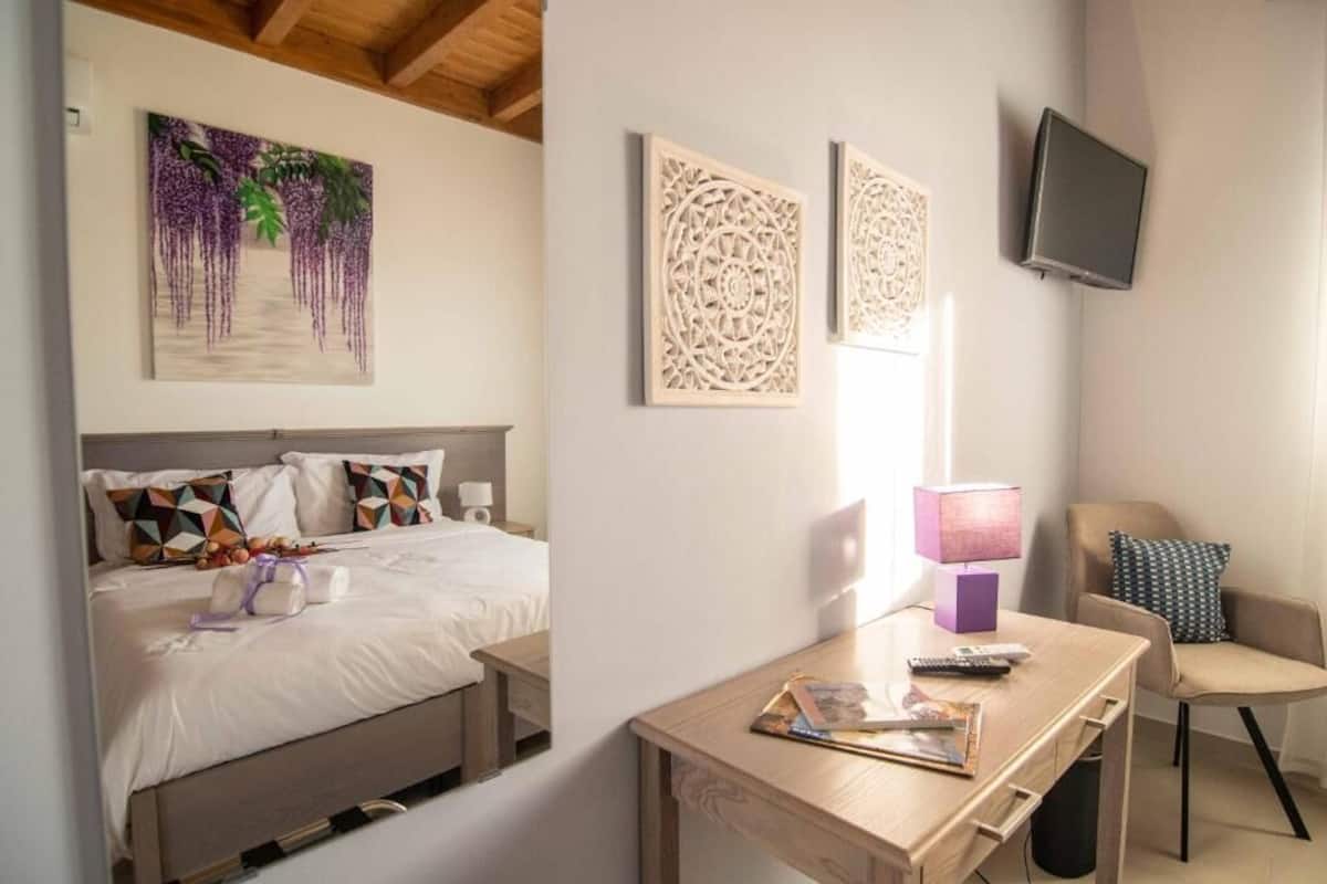 Une chambre dâhĂŽtel Ă©quipĂ©e dâun lit, dâun bureau, dâune tĂ©lĂ©vision et ornĂ©e dâĆuvres dâart sur les murs.