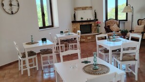 Comedor con mesas y sillas blancas, una chimenea y un ventilador de techo.